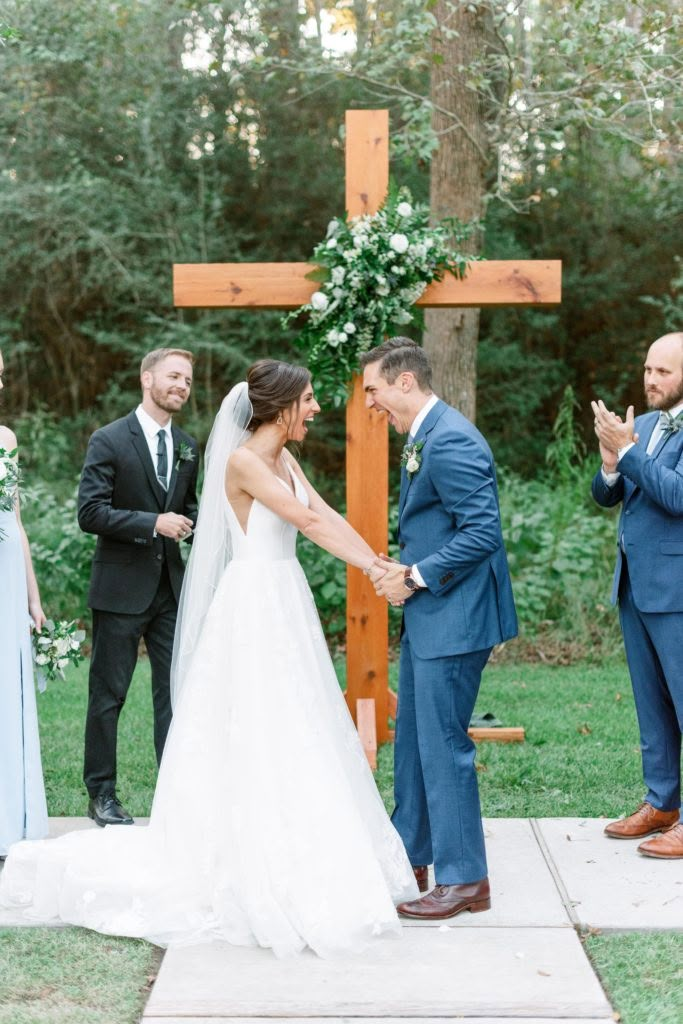 a bride and groom holding hands during their wedding ceremony in front of a wooden cross