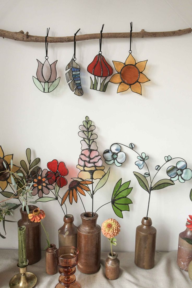 several vases with flowers in them are hanging on a wall next to a branch