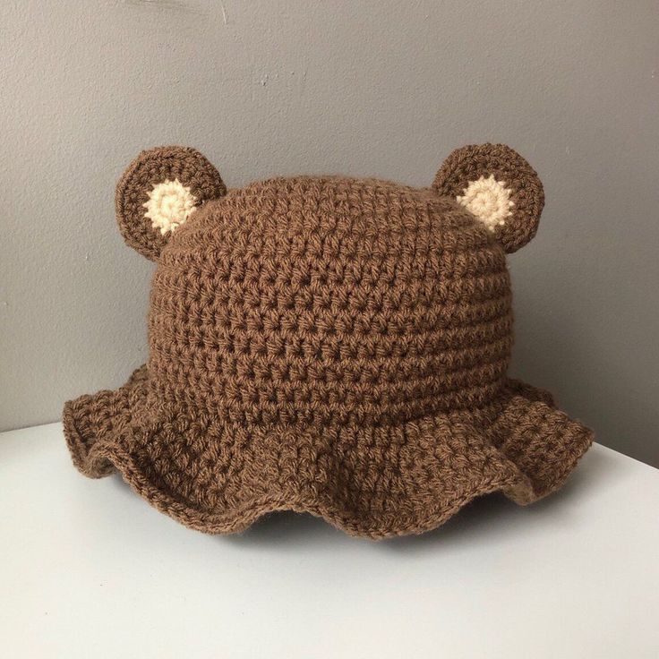 a brown crocheted hat with ears on top of a white table next to a gray wall