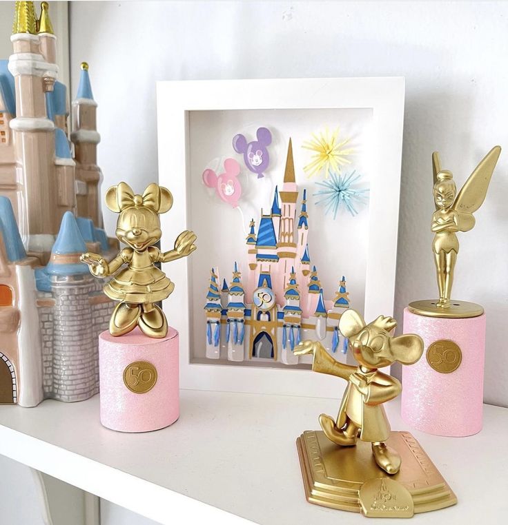 two gold mickey mouse figurines on a white shelf next to a pink castle