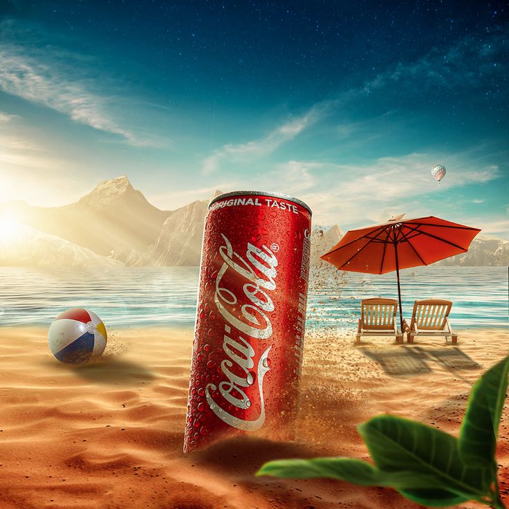 a can of coca - cola sitting on top of a sandy beach next to an umbrella