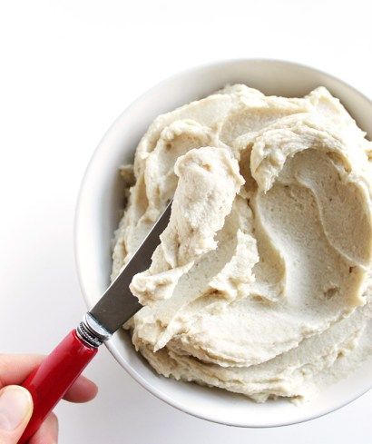 a hand holding a knife over a bowl of mashed potatoes with cream on top