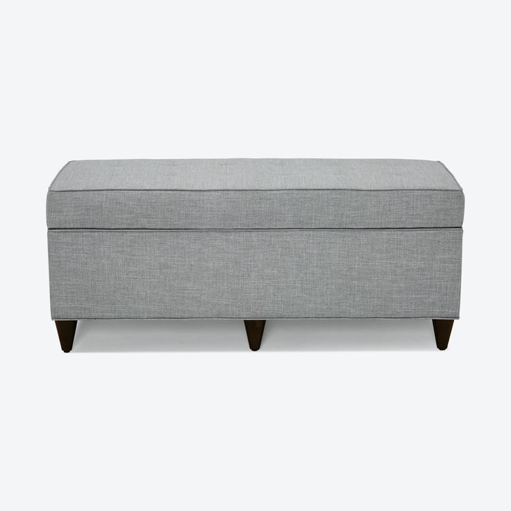 a gray bench with wooden legs and a cushion on the bottom, in front of a white background