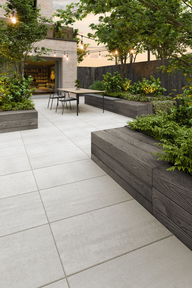 an outdoor dining area with tables and benches surrounded by greenery, trees and shrubs