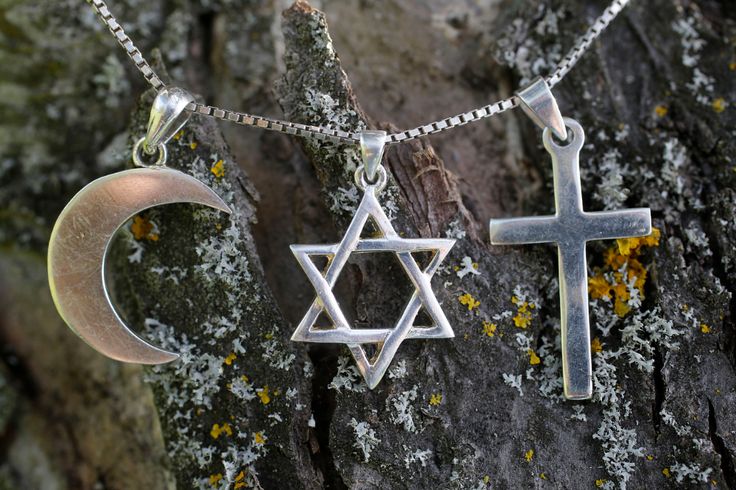 two silver crosses and a crescent hanging from a chain on top of a tree trunk