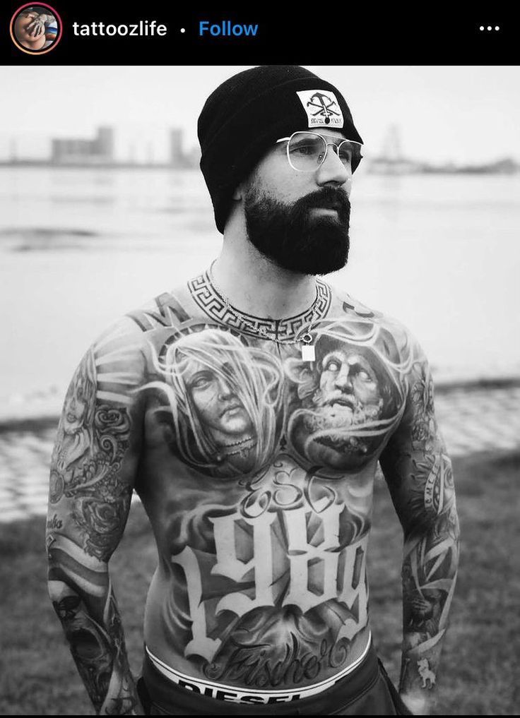 a man with tattoos on his chest standing next to the water