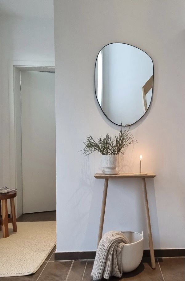 a mirror on the wall above a small table with a candle and potted plant