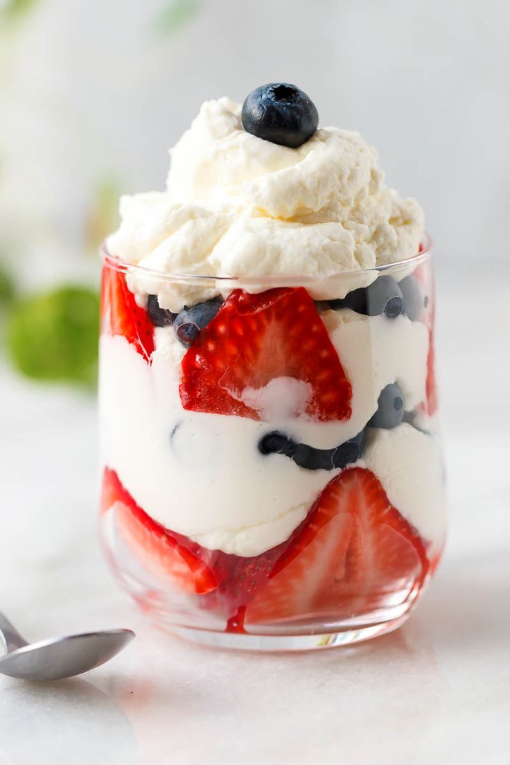 a dessert with strawberries, blueberries and whipped cream in a glass bowl on a table