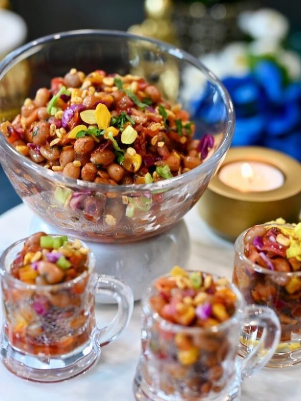 a glass bowl filled with lots of food on top of a table next to two cups