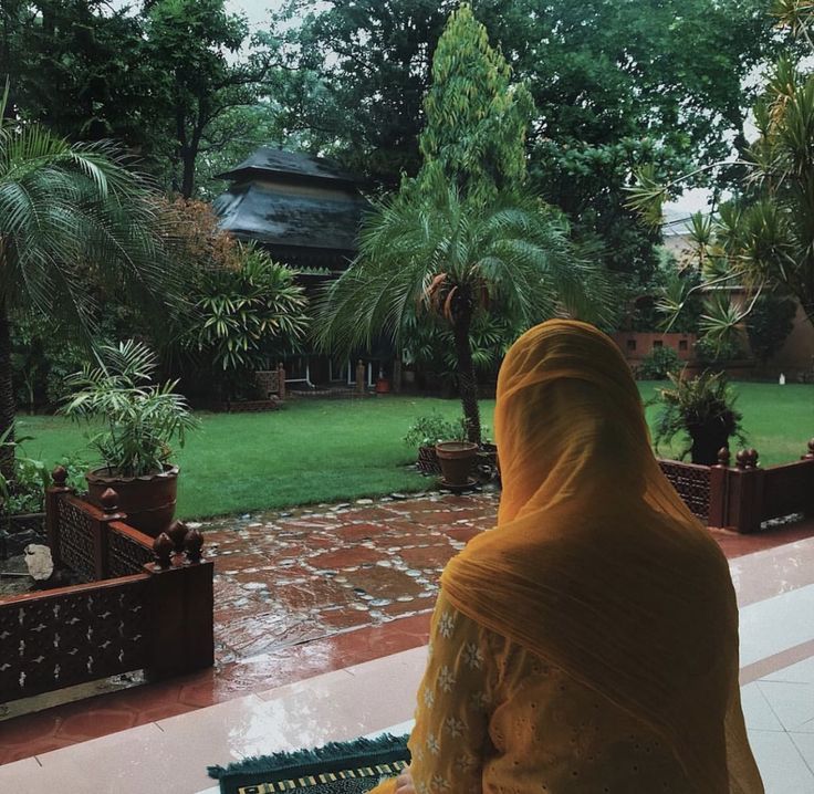 a woman sitting on a bench in front of a lush green yard