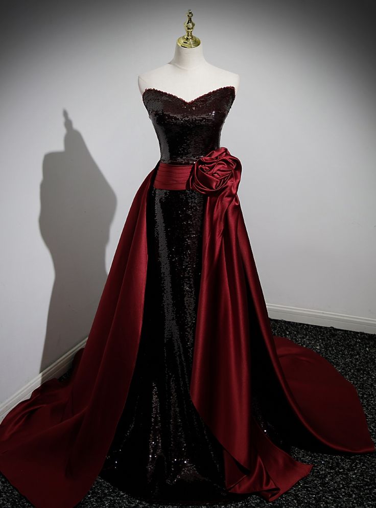 Brought to life with a cascade of sequins, this enchanting black prom dress is the epitome of dark glamour. The gown boasts a flirtatiously straight neckline, transitioning into a sea of shimmering sequins that catch the light with every movement. Embraced at the waist by a wide wine-red satin sash that blooms into an extravagant rosette, the dress spills into a sweeping train that trails with a silent promise of elegance. This garment isn't just a dress; ita centerpiece, a conversation starter, and a treasure that will shine in photos and memories alike. Red Dress Vampire, Black And Red Prom Dress, Vampire Life, Sequin Mermaid Prom Dress, Masquerade Outfit, Prom Dress Burgundy, Flower Prom Dress, Red Clothing, Mermaid Prom Dresses Lace