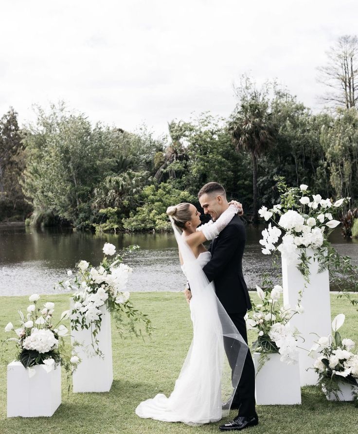 a bride and groom kissing in front of white floral arrangements on the grass at their wedding