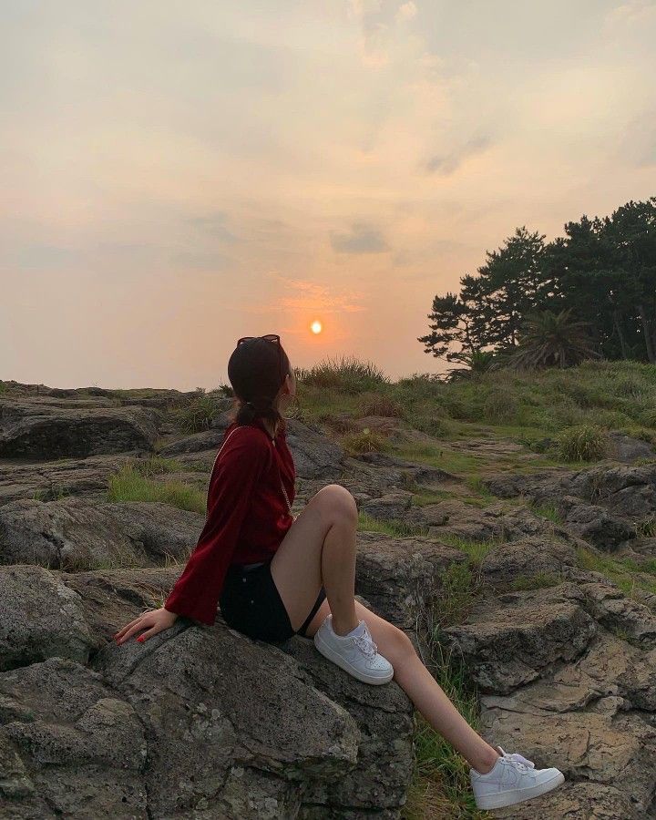 a woman sitting on top of a rock next to the ocean at sunset or dawn