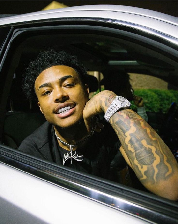 a man sitting in the passenger seat of a car with tattoos on his arm and wrist