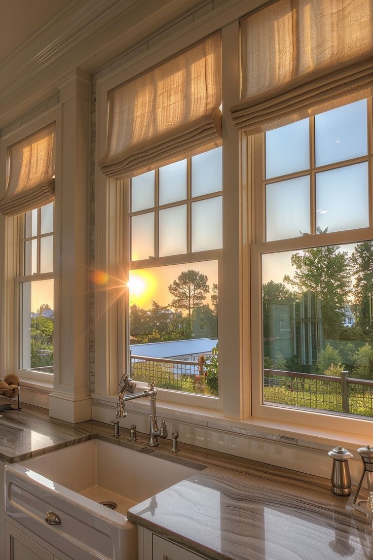 the sun shines through two windows in a kitchen with marble counter tops and white cabinets