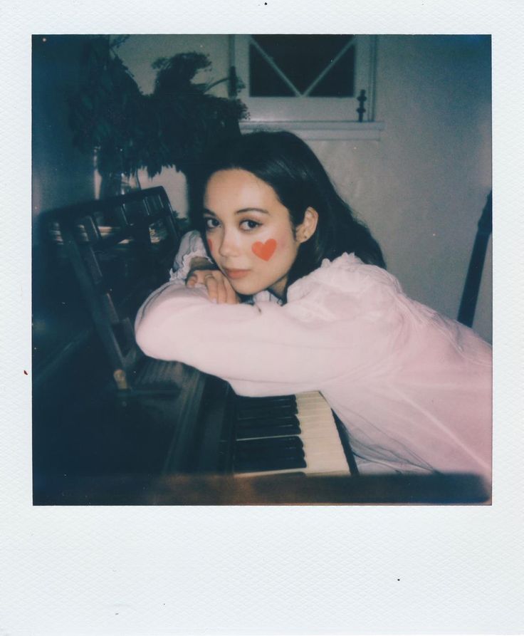 a young woman sitting at a piano with an orange nose painted on her cheek