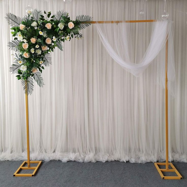 a wedding arch decorated with white flowers and greenery for a ceremony or reception in front of a drape curtain