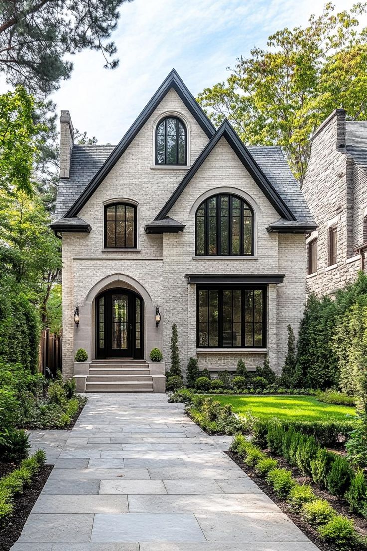 a white house with black windows and lots of greenery in the front yard area