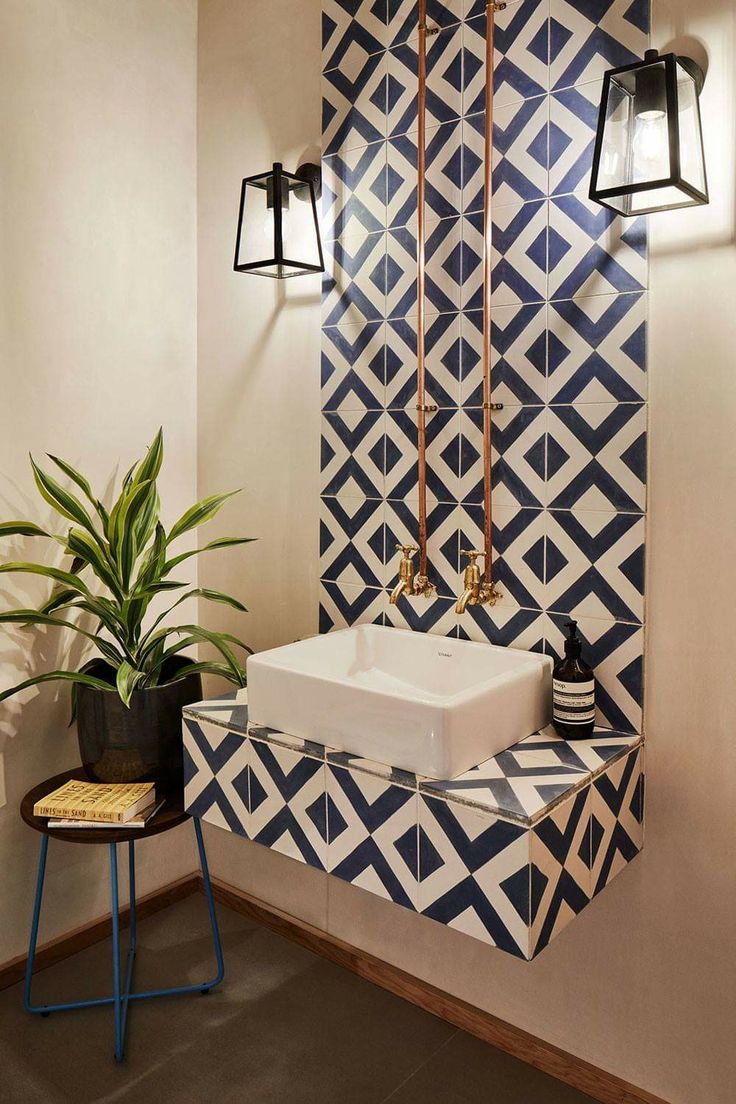 a bathroom with a sink, mirror and plant in it next to a tiled wall