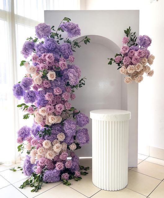 purple and white flowers are arranged on the wall next to a trash can