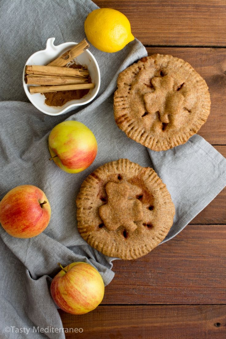 apples, cinnamon sticks and two pies on a table