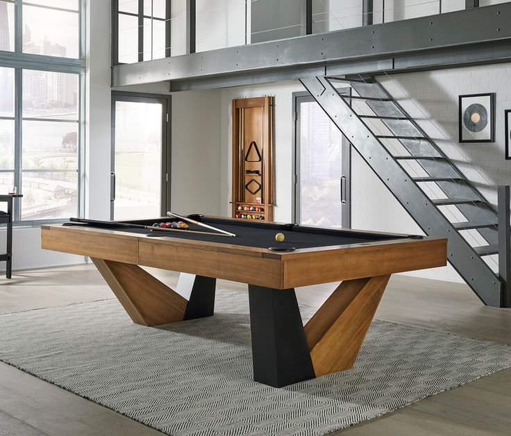 a pool table in the middle of a living room with stairs leading up to it