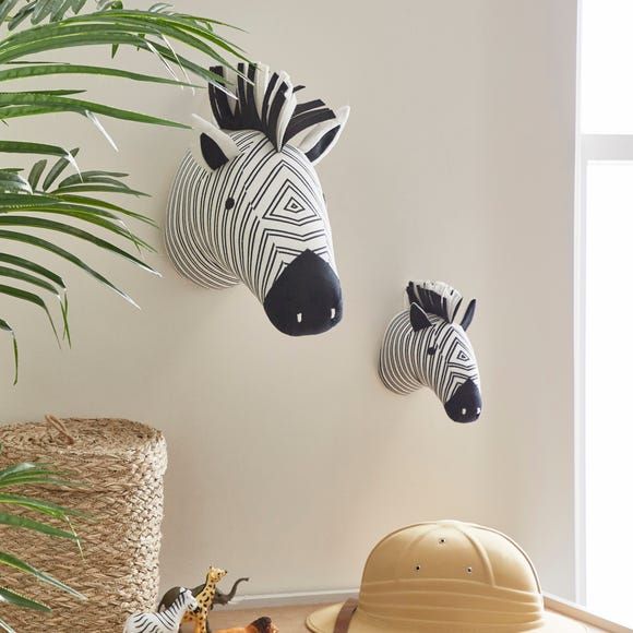 two zebra head mounted to the side of a wall next to a potted plant