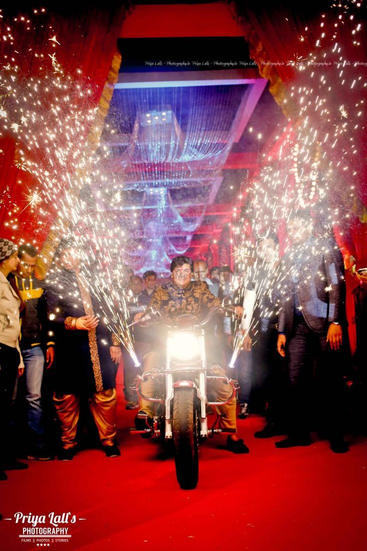 a man riding on the back of a motorcycle down a red carpeted floor covered in fireworks