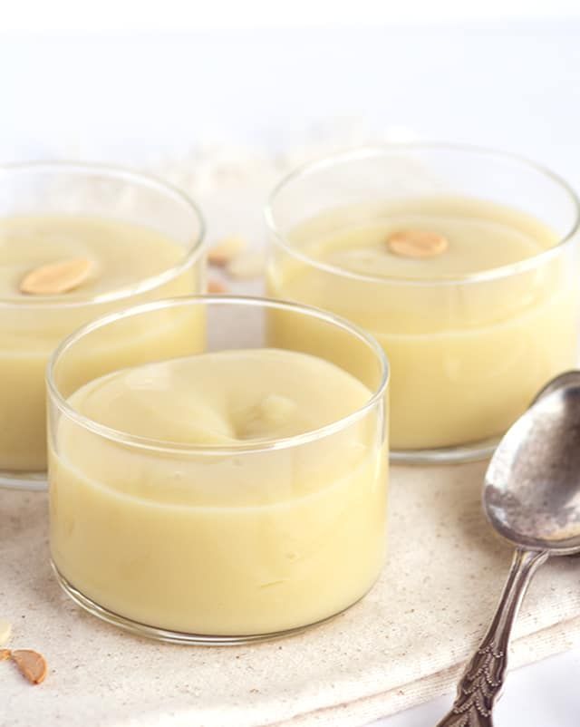 three glasses filled with pudding sitting on top of a table next to spoons and two bowls