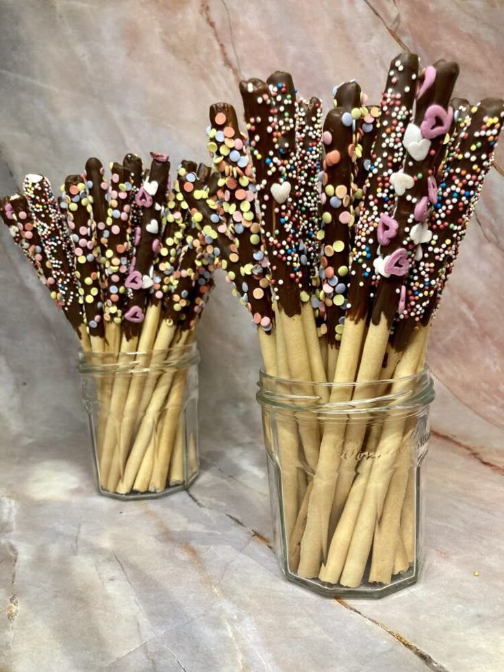 chocolate covered pretzel sticks with sprinkles in a glass jar on a marble surface