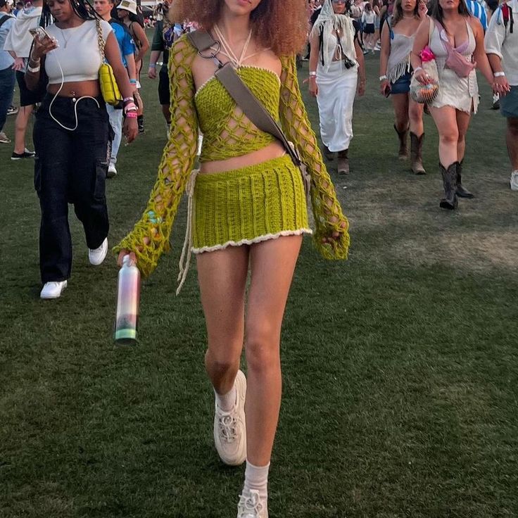 a woman in a green dress walking on the grass with other people behind her at an outdoor music festival