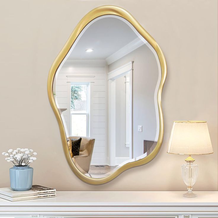 a mirror sitting on top of a white dresser next to a lamp and vase with flowers