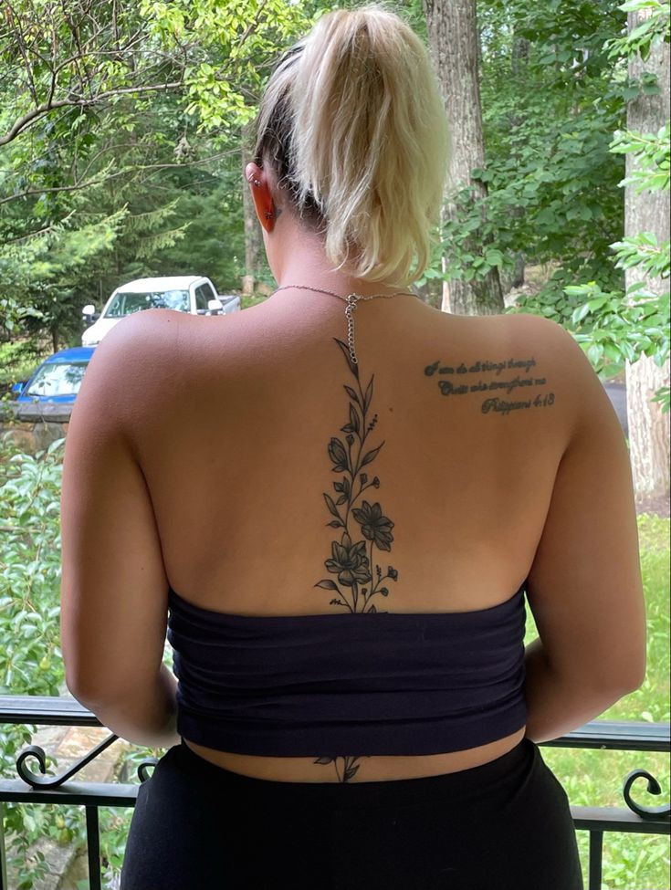 a woman with tattoos on her back standing in front of a fence and looking at the woods