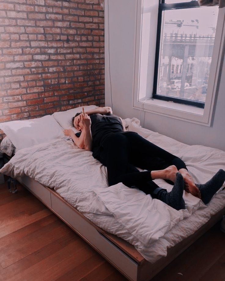 a person laying on top of a bed in a room with brick walls and windows