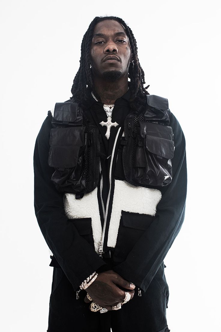 a man with dreadlocks standing in front of a white background wearing a black jacket