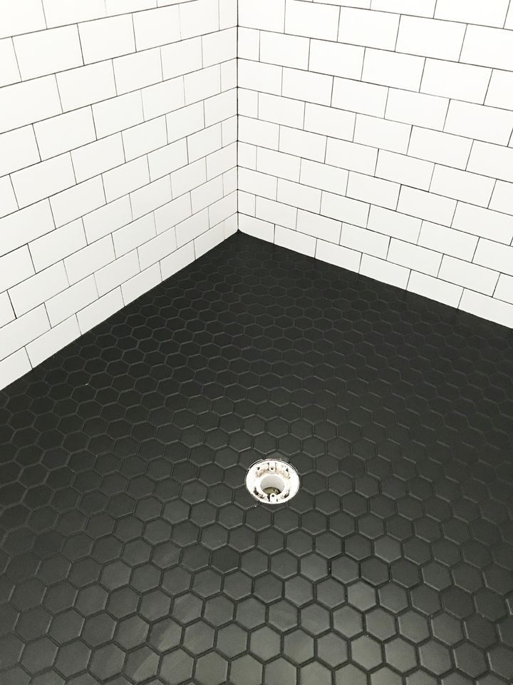 a black and white tiled shower stall with hexagonal floor tiles on the walls