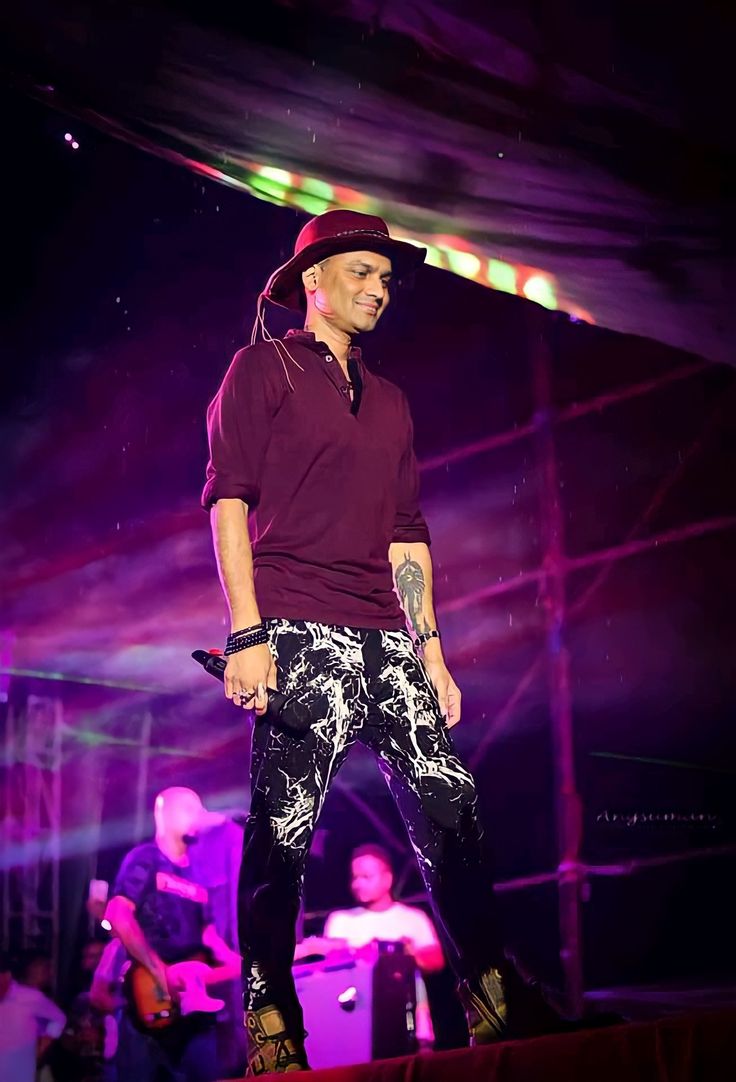 a man standing on top of a stage wearing black and white pants, a maroon shirt and a red hat