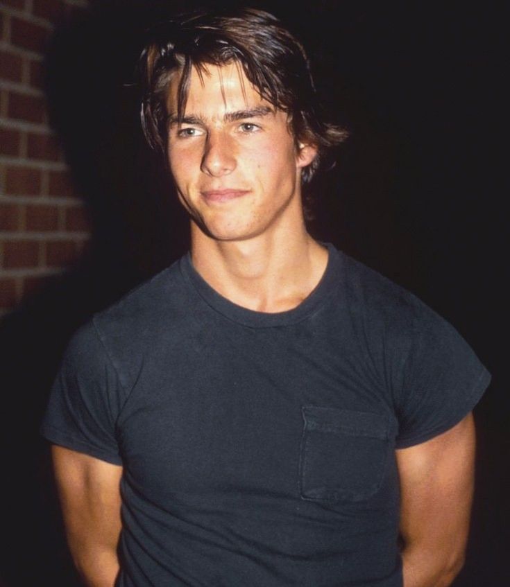 a young man is standing in front of a brick wall wearing a black t - shirt