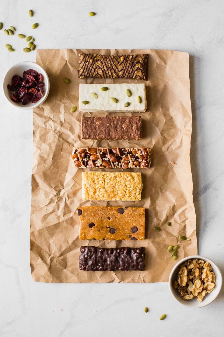 an assortment of desserts sitting on top of a piece of paper next to bowls of nuts