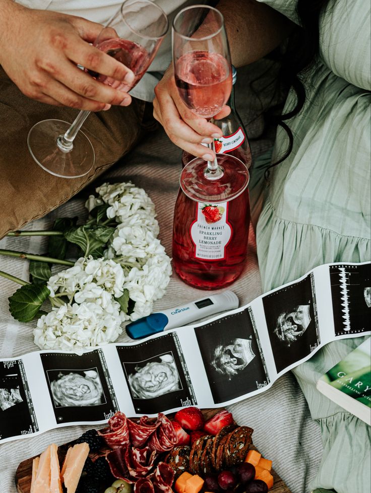 two people are toasting with wine and fruit on the table next to them,