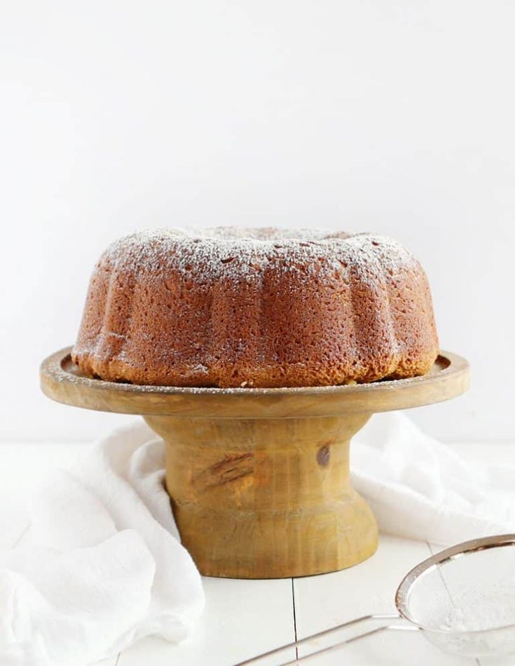 a bundt cake sitting on top of a wooden stand next to a pair of glasses