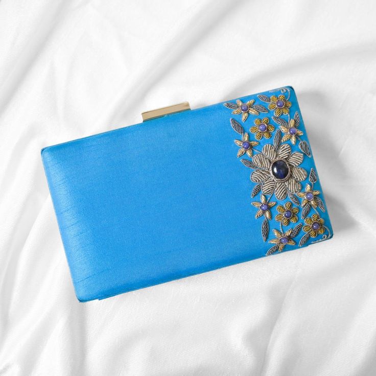 Featuring a sky blue zardosi floral clutch purse in silk base with onyx and metal thread embellishments, including a metal frame wrapped in silk and tablet clasp. Comes with satin lining and a gold chain. The floral clutch purse with intricate zardosi antique work gives a unique look to this luxury statement. Carry it with elegance in a wedding or evening party. Size: 20*12*4 Utility: Shoulder Bag, Hand Clutch Bag Material: Silk, Metal Zari Stones: Onyx Base Colors Available: Sky Blue Pocket: Single Zardozi comes from two Persian words: zar or zarin meaning 'gold', and dozi meaning 'sewing'. Embroidery with gold and silver threads has been prevalent in India since the times of Rigveda, and gained much popularity during the Mughal and its semblance in the form of Zardozi art, the intricate Blue Rectangular Evening Bag For Wedding, Blue Rectangular Evening Bag For Wedding Guest, Blue Embellished Evening Bag For Formal Occasions, Designer Rectangular Case Evening Bag, Blue Rectangular Clutch For Wedding Guest, Elegant Blue Clutch For Wedding Guest, Elegant Blue Evening Bag For Wedding Guest, Designer Rectangular Clutch For Events, Blue Elegant Clutch For Wedding Guest