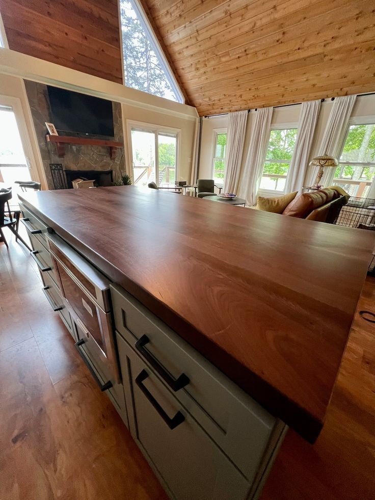 a large kitchen island in the middle of a wood floored living room with windows