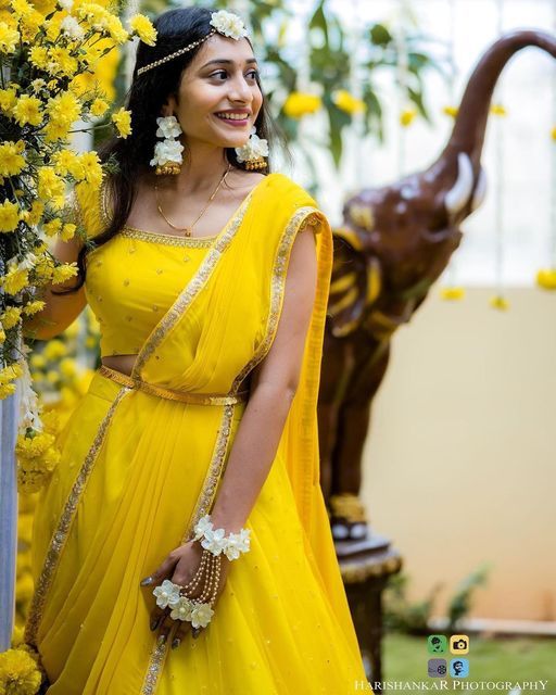 a woman in a yellow sari posing for the camera with flowers around her neck