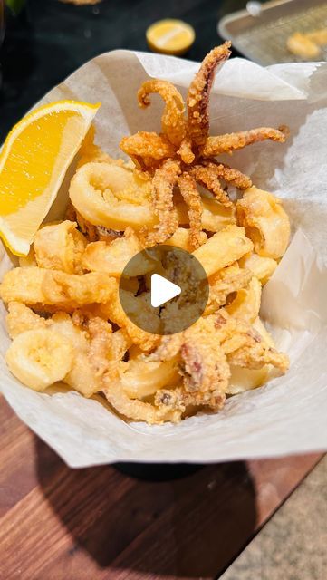 a bowl filled with fried food next to a slice of lemon