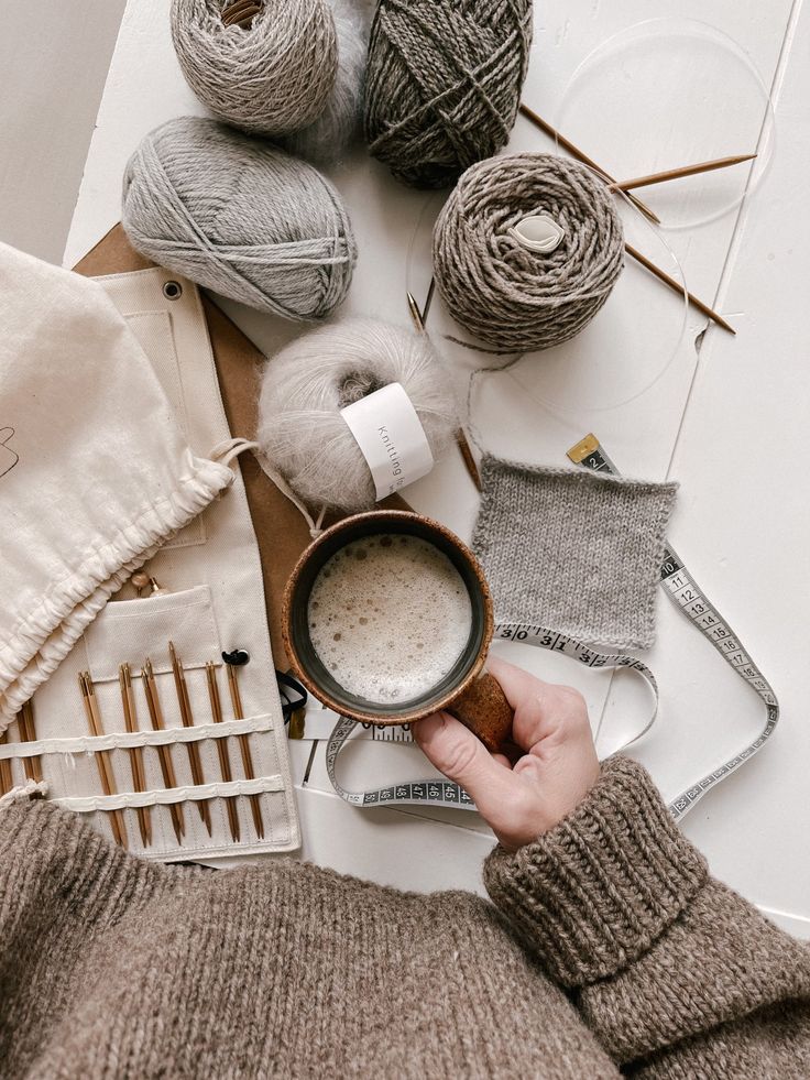 a person holding a cup of coffee in front of some knitting supplies