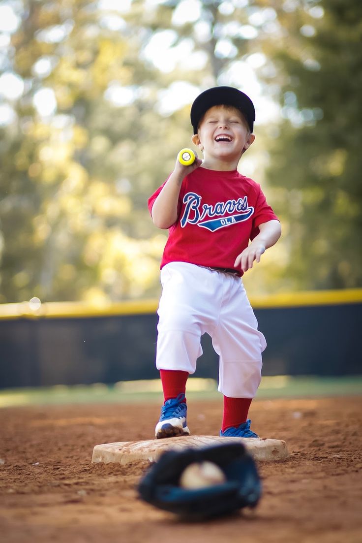 a young boy standing on top of a base wearing a baseball uniform and holding a ball