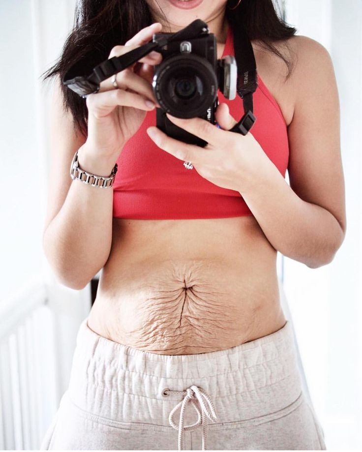 a woman in a red top holding a camera and taking a photo with her stomach