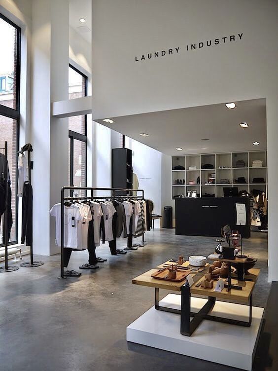 the inside of a clothing store with clothes on racks and tables in front of windows