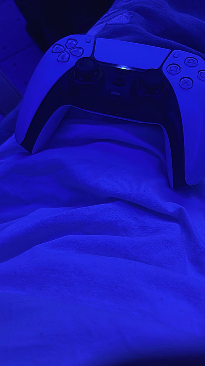 a close up of a video game controller on a bed with blue sheets in the background